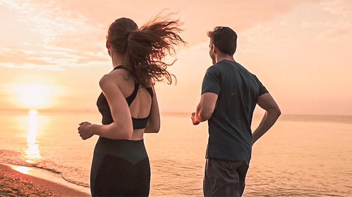 Kvinna och man joggar på stranden 